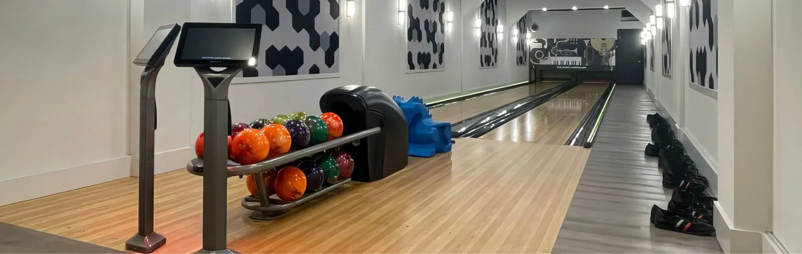 Two home bowling lanes with a ball return and a row of colorful bowling balls.